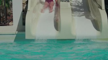 Genç kız neşeyle havuza su kaydırağından süzülüyor yavaş çekimde.