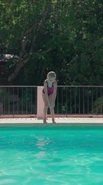 Gözlük takan genç bir kız, güneşli bir günde havuza atlıyor ve ağır çekimde filme alınıyor.
