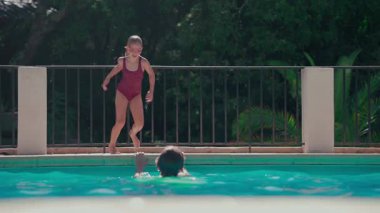 Genç kız neşeyle yüzme havuzuna atlıyor güneşli bir günde yavaş çekimde su sıçrıyor