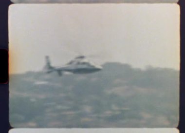 Klasik film dokusu, ince ışık kusurları ve gerçek bir nostaljik titreşim uyandırmak için kıvrımlı kenarları olan, sisli bir manzaranın üzerinde süzülen bir helikopter görüntüsü.