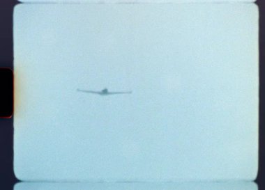 Otantik Süper 8 filmi, uzaktan yaklaşan bir hafif uçağı yakalıyor ve tam tepemizde uçuyor, düşük açılı bir perspektiften nostaljik ve kumlu bir estetik sergiliyor.