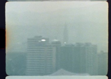 Otantik Super 8mm film görüntüleri sisli bir şehir siluetini, yoğun sis ve sislerin arasından zar zor görünen binaları, kentsel kirlilik ve atmosferik belirsizlik hissini aktararak yakalar.