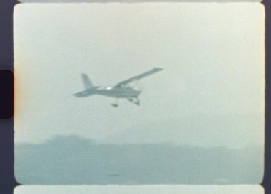 1970 'lerin arşivi, puslu bir şehir manzarasının üzerinde alçaktan uçan tek bir motorlu pervane uçağı gösteriyor. Nostaljik ve kumlu film estetiğini gösteriyor.