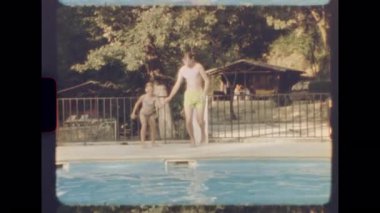 Erkek ve kız kardeş, güneşli bir günde havuza atlarken el ele tutuşuyorlar ve 8mm 'lik klasik bir filme çekiliyorlar.