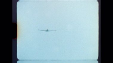 Otantik Süper 8 filmi, uzaktan yaklaşan bir hafif uçağı yakalıyor ve tam tepemizde uçuyor, düşük açılı bir perspektiften nostaljik ve kumlu bir estetik sergiliyor.