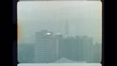 Otantik Super 8mm film görüntüleri sisli bir şehir siluetini, yoğun sis ve sislerin arasından zar zor görünen binaları, kentsel kirlilik ve atmosferik belirsizlik hissini aktararak yakalar.