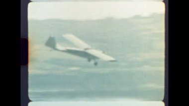 Orijinal, Otantik 8mm film kaydı. Nüfusun yoğun olduğu bir bölgeye inmek için zarif bir şekilde inen küçük bir uçağın gerçek ışık sızıntıları ve film tahıllarıyla nostaljik bir yolculuk görüntüsü.