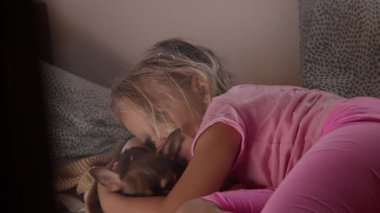 Pembe elbiseli genç kız sıcak bir nostaljik atmosferde küçük köpeğine sarılıyor.