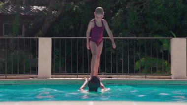 Mayo giymiş ve gözlüklü genç bir kız güneşli bir günde havuzda neşeyle zıplıyor ve sıçrıyor.