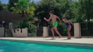 Yaz tatilinde havuza atlayan mayo giymiş güler yüzlü bir oğlan ve kız.