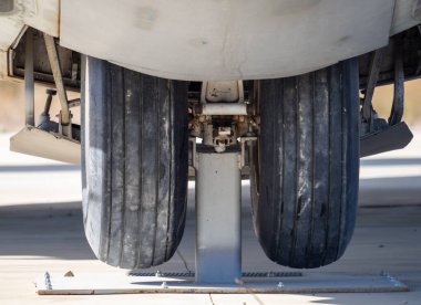 Açık havada gösterilen yıpranmış iniş takımı lastikleri ve korunmuş askeri uçağın süspansiyon yapısı.