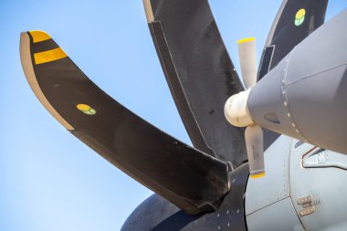 Açık gökyüzü altında bir askeri nakliye uçağının turbopervane motor beşiğine bağlı büyük, kompozit pervane bıçakları yakın çekim
