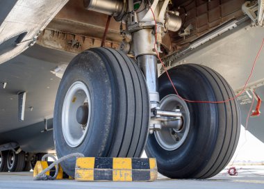 Çift tekerli ana iniş takımlarının zemin katındaki manzarası görülebilir körfez iç ve hidrolik montajları olan takozların üzerinde dinleniyor.