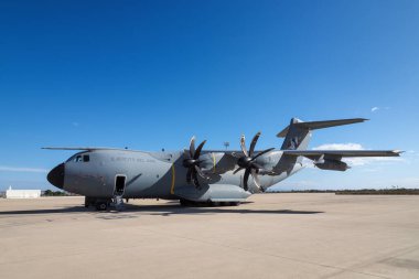 Askeri taktik hava aracı açık mavi gökyüzünün altında havaalanı önlüğüne park etmiş.