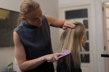 Bir kadın kapalı bir ortamda başka bir kadının saçını tarar, saç bakımına ve bakım tekniklerine odaklanır..