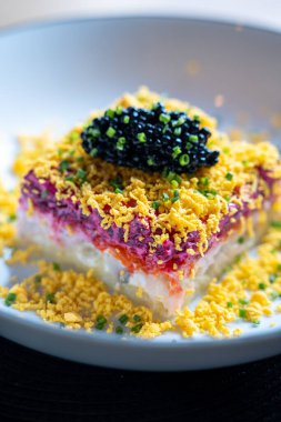 Siyah havyarla kaplanmış canlı bir salataya yakın plan. Beyaz bir tabakta soğan ve yumurta parçacıklarıyla süslenmiş..