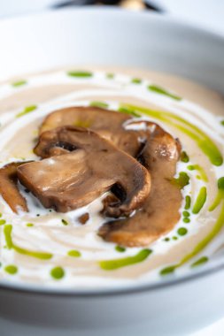 Mantar dilimleri ve yeşil yağ damlalarıyla süslenmiş kremalı mantar çorbasını yakından çek..