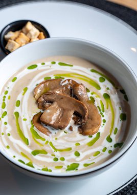 Lezzetli kremalı mantar çorbası. Yanında taze otlar ve kızarmış ekmeklerle servis ediliyor.