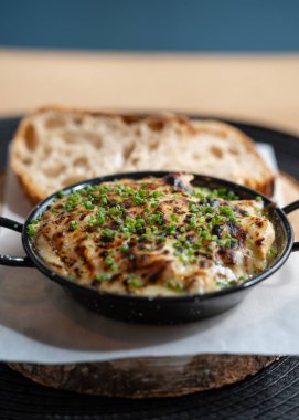 Lezzetli fırınlanmış peynir tabağı taze doğranmış soğanla kaplı siyah tavada servis edilen kabuklu ekmek..