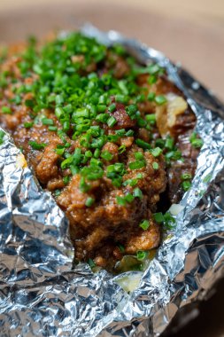 Üzerinde lezzetli et ve ahşap bir yüzey üzerinde taze soğan bulunan folyoya sarılı fırında patatese yakın plan..