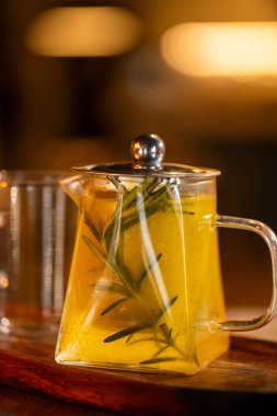 Sıcak ortam aydınlatmasıyla tamamlanmış ahşap bir yüzeye yerleştirilmiş taze biberiye içeren şeffaf cam çaydanlık..