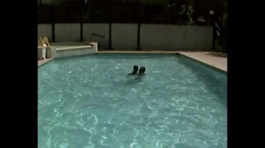 Açık havada yüzme havuzunda sırt üstü yüzen kızlarıyla babalarının geniş bir görüntüsü.