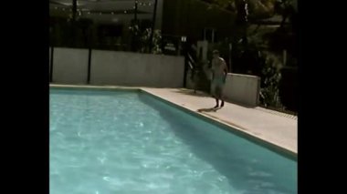 Çocuk açık havuzda su altında süzülüyor. Kolları açık ve parlak güneş ışığı altında.