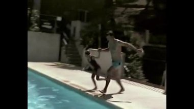 Yüzme havuzu kenarına koşarken el ele tutuşan kardeşler.