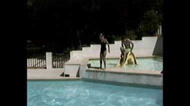 Kız ve erkek, açık havuzun sığ alanındaki küçük sarı su kaydırağının yanında.