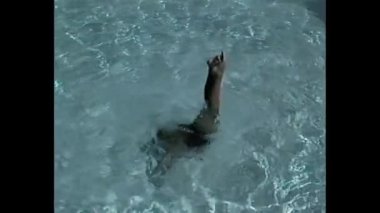 Suya batmış, bacakları açık bir yüzme havuzunda kalmış küçük bir çocuk.