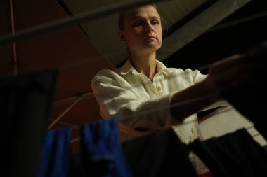 Düşük perspektifli bir bakış açısıyla bir kadının gece boyunca hafif ışıkla çamaşırlarını askıya koyması.