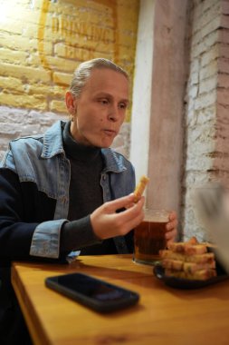 Kişi ahşap bir masada oturur ve sıcak bir kafede bir bardak bira ve atıştırmalıkların tadını çıkarır.