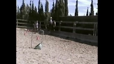 Kum eğitim alanında koni yanında ata binen çocuk VHS tarzında filme alınır.
