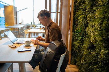 Man sitting at a cafe table with a laptop and a cup of coffee enjoying a snack