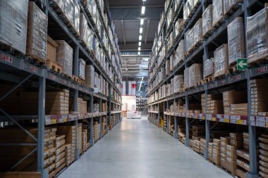 Yüksek tavanlı ve parlak ışıklandırmalı büyük bir endüstriyel depoda raflar dolusu kutu ve paletler..