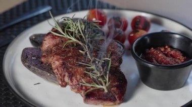 Biberiye filizi ile kaplanmış füme biftek servis sırasında aromatik dumanı serbest bırakıyor.