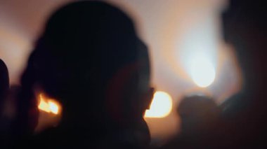 Seyirci siluetleri canlı konser sırasında müzik enerjisi ve kalabalık heyecanını ifade eden sıcak sahne ışıklarıyla el kaldırılır.