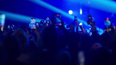 Kalabalık, yoğun ışıklandırma ve heyecan verici müzik atmosferiyle konser kaydetmek için akıllı telefonları yükseltiyor.