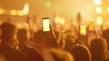 Kaldırılmış el telefonu, parlak sahne ışıklarını yakıyor ve canlı müzik performansı sırasında coşkulu bir şekilde tezahürat yapıyor.