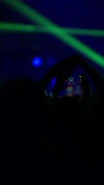 Kalabalık izleyiciler karanlık sahnenin altında dans ediyor. Parlak flaş ışıkları dramatik canlı müzik sahneleri yaratıyor.