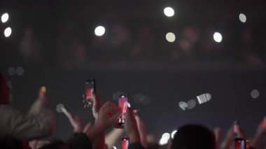 Kaldırılmış eller ve akıllı telefonların yakın görüntüsü kalabalığın içinde flaş ışık darbeleri olarak duygusal canlı müzik performansı kaydediyor.