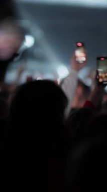 El kameraları ön planda tutarak flaş ışığı ve hareketli kalabalıkla dinamik canlı müzik performansı kaydediyor.