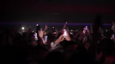 Siluetli kalabalık, canlı müziğe tepki veren el ve telefonları kaldırıyor. Işıklar mekanı kasıp kavururken güçlü bir konser ortamı yaratıyor.
