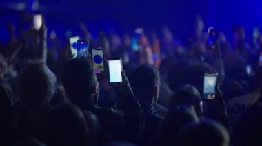 Yavaş çekim kalabalık dans ediyor ve canlı konser çekiyor. Parlak sahne ışıkları titreşiyor ve kolektif enerjiyi arttırıyor.