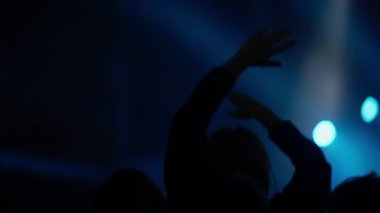 Karanlık kalabalık siluetleri, flaş ışığı ve yoğun konser atmosferi altında canlı müzik anının doruğunu kutlayan el ve telefonları kaldırıyor.