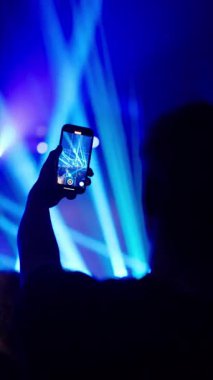 Seyirciler, canlı bir gece kulübü atmosferi yaratan mavi sahne ışıkları ve lazer ışınlarıyla akıllı telefon kayıt konseri düzenliyor.