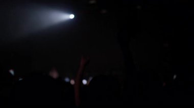 Siluetli kalabalık canlı konser sırasında sahne ışıklarıyla el kaldırıyor duygusal atmosfer ve birlik hissi yaratıyor.