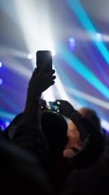 Seyircilerin parlak akıllı telefon ekranları ve ışıklarıyla canlı performansı çektikleri dikey görüntüler