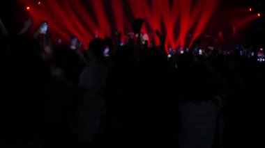 Seyirciler ağır çekimde el ve akıllı telefonları kaldırırken, sahne ışıkları canlı müzik performansını aydınlatıyor.