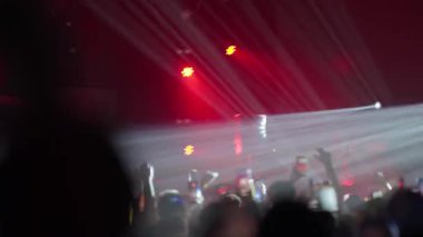 Canlı müzik konserindeki seyircilerden görüntüler. Siluetli kalabalık kırmızı ve beyaz sahne ışıkları yanıp sönerken kaydetmek için telefonları tutuyor. Enerjik, titrek kamera büyüleyici bir festival deneyimi yarattı.